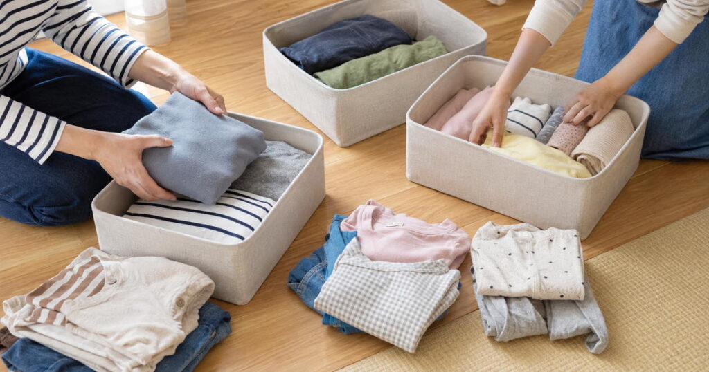 床に広げた家族の服を収納ボックスへ分けている手元